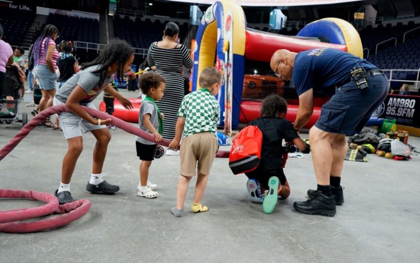 Firefighter showing a group of children a fire hose.